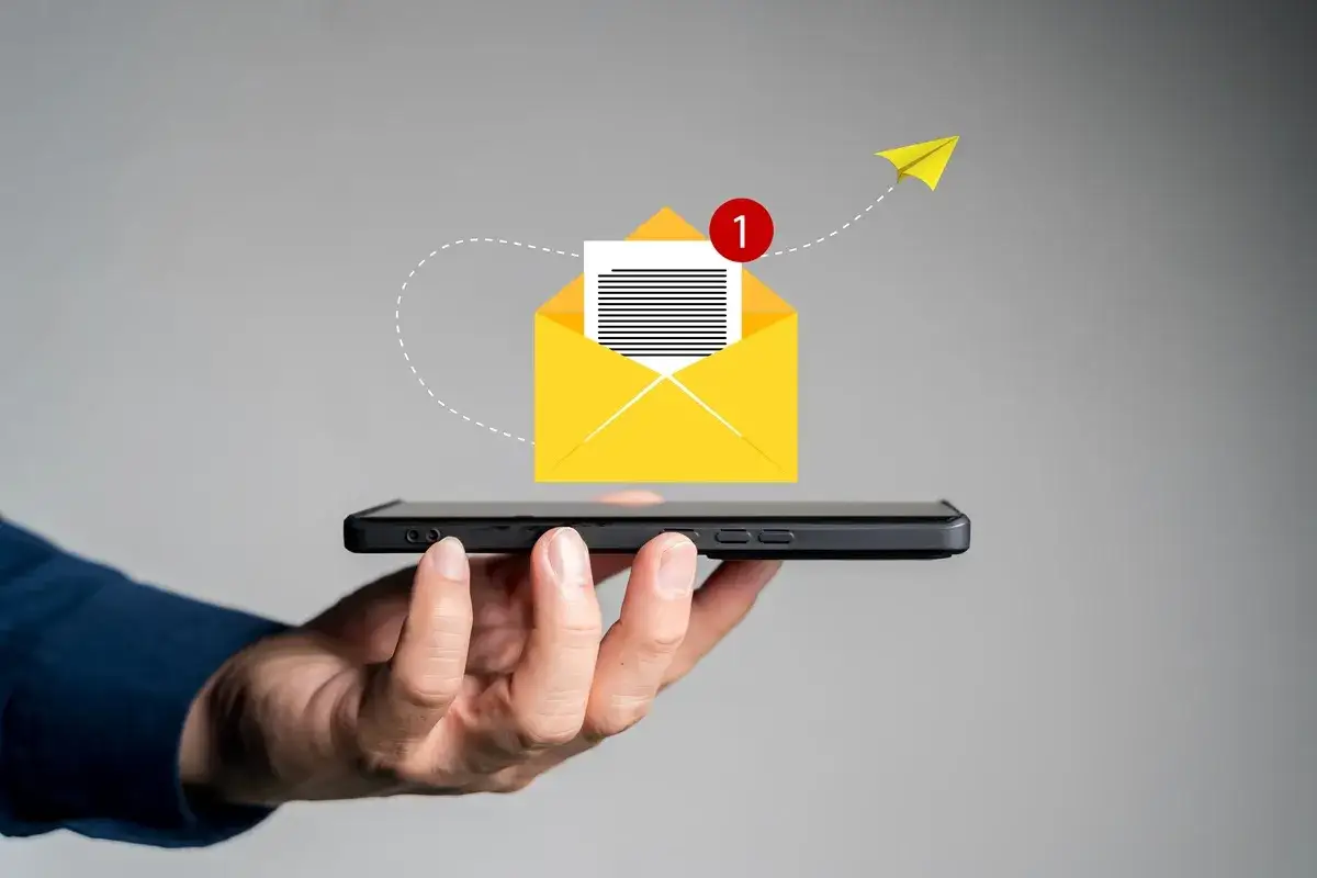 Dłoń trzyma smartfon, z którego wylatuje żółta koperta z powiadomieniem. Jak napisać smsa o urlop na żądanie?