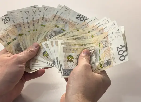 Dłonie trzymają wachlarz banknotów 200 zł. Zastanawiasz się, ile to brutto, jeśli 4200 netto to Twoja pensja?