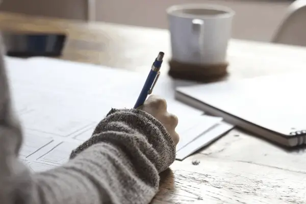 Ręka pisze na papierze, obok kubek kawy. Zastanawiam się, czy to formularze ZUS, czy może coś innego? ZFA co to jest?